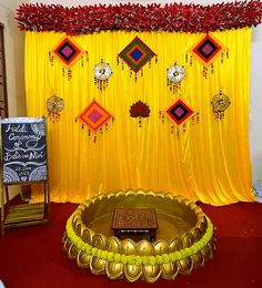 a decorated stage with yellow drapes and red flowers on the wall, along with a gold bowl