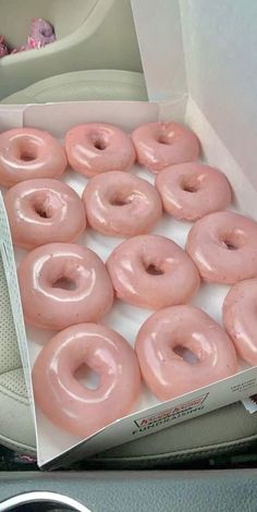 a box filled with pink frosted donuts sitting on top of a car seat