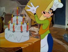 an animated mickey mouse holding a large box with candles on it's face in front of a birthday cake