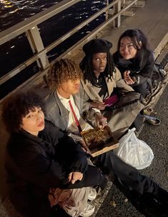 four people are sitting on the sidewalk eating food