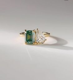 an emerald and diamond ring with two pear shaped diamonds in the center, on a white surface