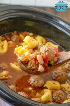 a ladle full of soup with meatballs and pasta in the slow cooker