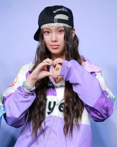 a young woman making a heart sign with her hands while wearing a hat and jacket