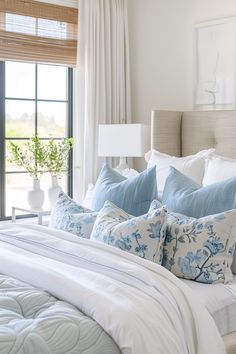 a bed with blue and white pillows on top of it next to a large window