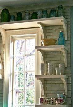 a kitchen with white shelves filled with dishes and cups next to a window sill