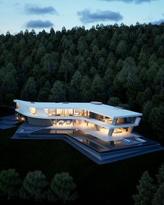 an aerial view of a modern house in the middle of trees at night with lights on