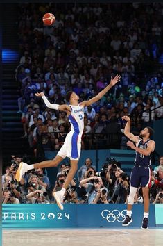 two men playing basketball in front of a crowd with cameras on the sidelines watching