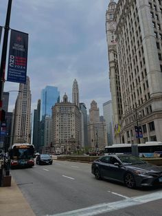 cars are driving down the street in front of tall buildings and skyscrapers on a cloudy day