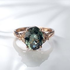 a ring with a green stone and two diamonds on it's sides, sitting on a white surface