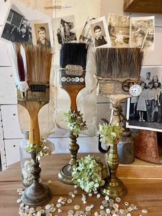 three vases with flowers and brushes sitting on top of a wooden table next to pictures