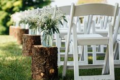 white chairs and vases with flowers on them are lined up in the grass near a tree stump