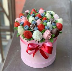 a pink hat box filled with lots of different types of berries and chocolate covered strawberries