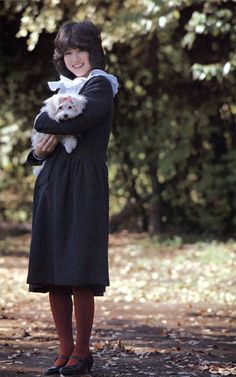 a woman holding a cat in her arms while standing next to trees and leaves on the ground