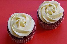 two cupcakes with white frosting sitting on a red surface