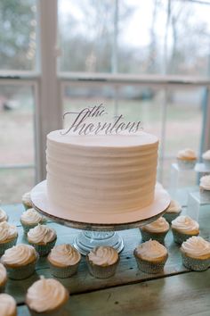 a cake and cupcakes sit on a table in front of a large window