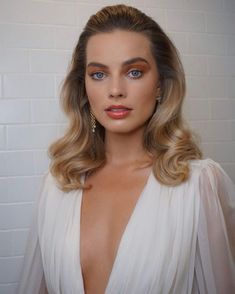 a woman with blonde hair and blue eyes wearing a white dress in front of a brick wall