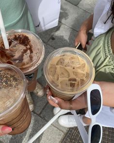 three people are holding up iced coffees in their hands