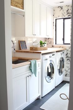 a washer and dryer in a white kitchen with floral wallpaper on the walls