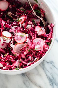 a bowl filled with red cabbage and radishes on top of a marble counter