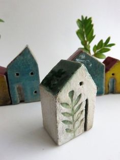 small ceramic houses with plants growing out of them on a white surface, next to each other