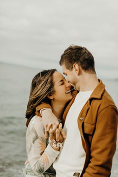 a man and woman standing next to each other near the ocean