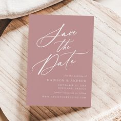 a pink save the date card sitting on top of a wooden table next to a white plate