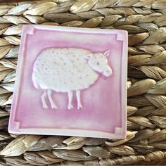 a pink plate with a white sheep on it sitting on a woven basket next to some straw