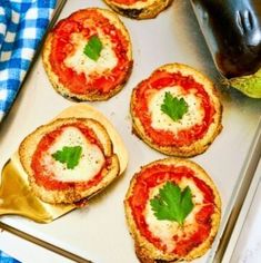 mini pizzas with cheese and tomato sauce are on a baking sheet next to a bottle of ketchup