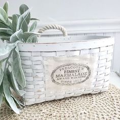 a white basket sitting on top of a table next to a plant