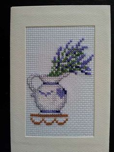 a cross stitch picture of a blue and white vase with purple flowers in it on a black background