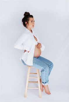 a pregnant woman sitting on top of a wooden stool