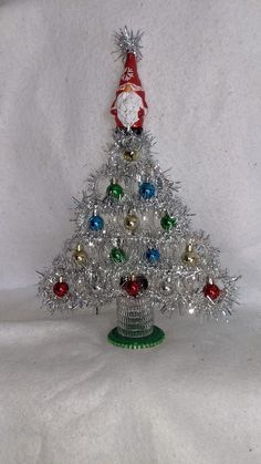 a small silver christmas tree sitting on top of a white table covered in tinsel