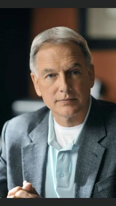 a man in a suit sitting down with his hands folded and looking off to the side