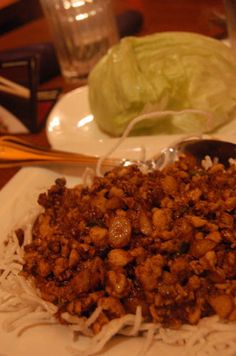 a white plate topped with meat covered in sauce next to a lettuce leaf