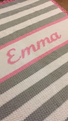 a crocheted baby blanket with the name 3mna written on it in pink and grey stripes