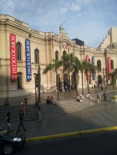 people walking in front of an old building with palm trees on the street and stairs leading up to it