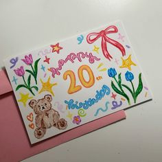 a happy 20th birthday card with a teddy bear and flowers on the front, next to a pink envelope