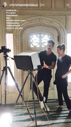 a man and woman standing next to each other in front of a camera on a tripod