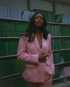 a woman in a pink suit standing next to a book shelf filled with green books