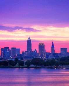 the city skyline is lit up at sunset with pink and purple clouds in the background