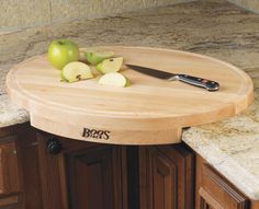 a wooden cutting board sitting on top of a counter next to a knife and some apples