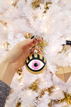 a hand holding an ornament in front of a white christmas tree with ornaments