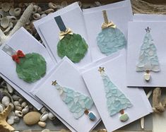 four cards with christmas trees on them and seashells in the sand behind them