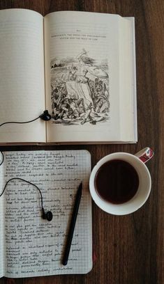 an open book sitting on top of a wooden table next to a cup of coffee