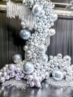 an arrangement of silver balls and streamers on a black table with curtains in the background