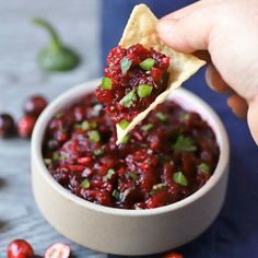 a hand holding a tortilla chip with cranberry salsa