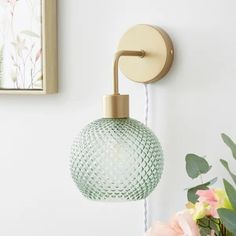 a light that is on the side of a wall next to a vase with flowers