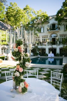 a table with flowers and champagne glasses on it in front of a large house that has a swimming pool