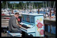 a man sitting on top of a blue piano next to a harbor filled with boats