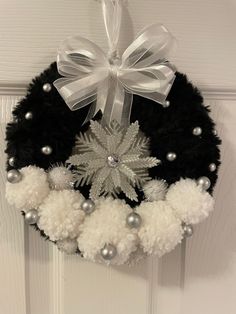 a black wreath with white pom - poms and silver balls hanging from the front door